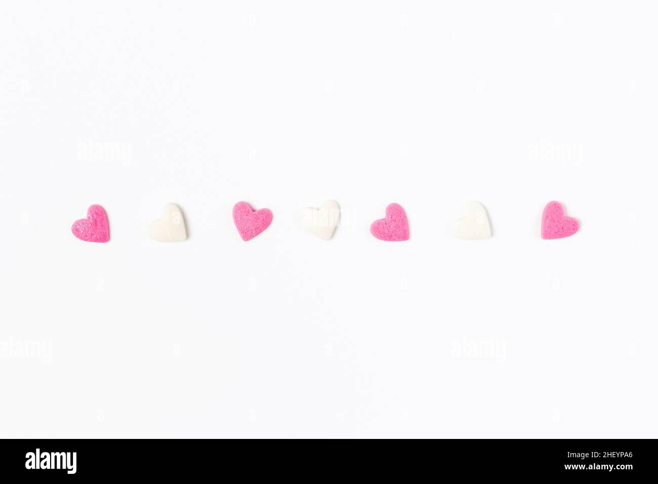Pink and white heart-shaped sugar candies on white background, minimalistic saint valentine`s day greeting card Stock Photo